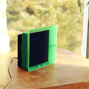 Könnte beinhalten: Ein grüner und schwarzer 3D-gedruckter Ventilator mit einem schwarzen Filter. Der Ventilator steht auf einem Holztisch.