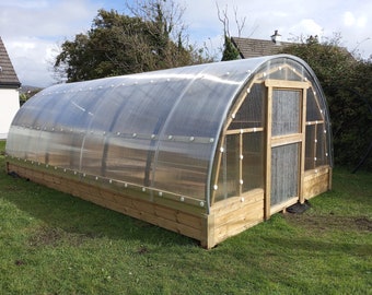 May include: A wooden framed greenhouse with a clear plastic roof and a wooden door. The greenhouse is sitting on a wooden platform.
