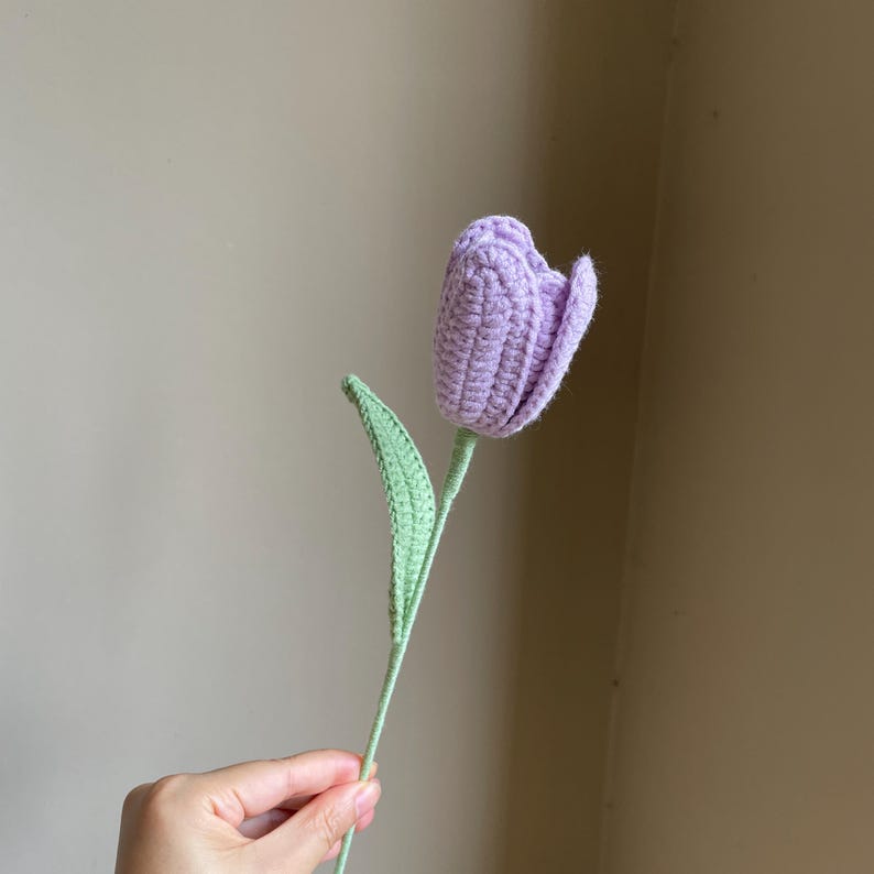 May include: A handmade crochet tulip in shades of lavender and green. The flower head is a soft lavender, with detailed stitching. The stem and leaf are a light green. A unique, handcrafted floral decoration.