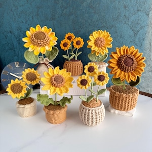 May include: A selection of handmade crochet sunflowers in various sizes, each potted in a unique crocheted container. The sunflowers have yellow petals, brown centres, and green leaves. The pots are in shades of beige and orange.