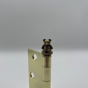 Può includere: Una cerniera per porta dorata con una piccola statuetta di orsacchiotto dorata in cima.