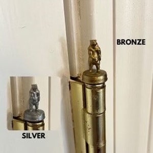 May include: Two door hinges with decorative bear finials. The bear on the left is silver and the bear on the right is bronze.