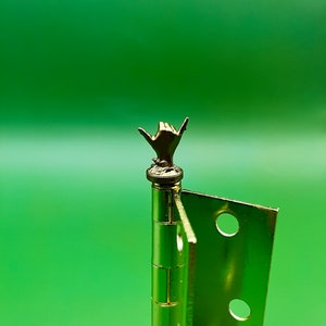 May include: A gold door hinge with a decorative hand-shaped finial. The finial is in the shape of a hand giving the shaka sign.