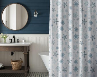 Puede incluir: Cortina de ducha blanca con un estampado de copos de nieve azules. La cortina está en un baño con una pared azul oscuro, un espejo redondo y una bañera blanca. El baño tiene un tocador de madera rústica.