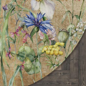 May include: A round rug featuring a watercolour design of assorted flowers and plants on a gold background. The flowers include blue, pink, yellow, and white blooms.