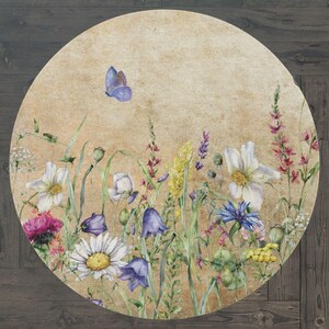 May include: A round rug with a vintage floral design. The rug features a variety of flowers in shades of blue, pink, white, and yellow, as well as a butterfly in the top left corner. The background is a light beige with a textured look.
