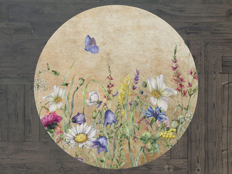 May include: A round rug with a vintage floral design. The rug features a variety of flowers in shades of blue, pink, white, and yellow, as well as a butterfly in the top left corner. The background is a light beige with a textured look.