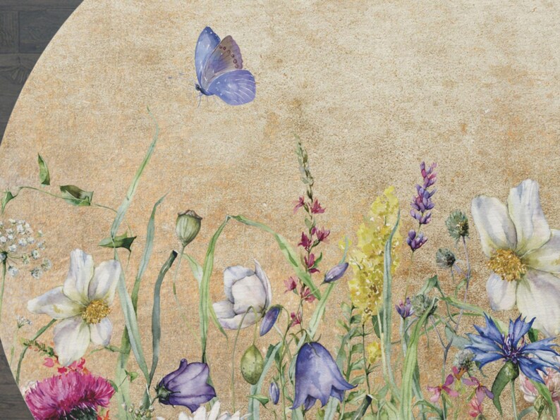 May include: A watercolour painting of a round floral arrangement with a light brown background. The arrangement features a variety of flowers, including white daisies, purple bellflowers, blue cornflowers, and yellow wildflowers. A single blue butterfly is flying above the flowers.