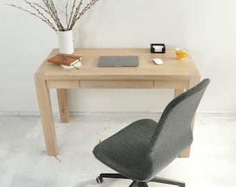 Op de afbeelding: Een licht houten bureau met een laptop, een notitieboek, een pen, een witte draadloze muis, een klein zwart dienblad en een gele mok. Een grijze bureaustoel met zwarte wielen staat voor het bureau.