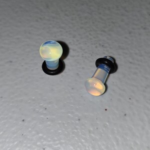 May include: Two opalite ear gauges, one with a black o-ring and one without. The gauges are a light blue and white color.
