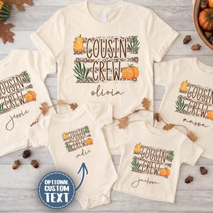 May include: A collection of cream-colored t-shirts and a baby bodysuit featuring a graphic print with the text "COUSIN CREW" in brown letters, accompanied by illustrations of orange pumpkins and green leaves, with personalized names printed below each design.