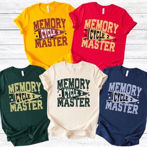 May include: Five short-sleeved t-shirts in various colors: yellow, red, dark green, cream, and navy blue. Each shirt features the text "MEMORY CYCLE 2 MASTER" in a distressed, vintage style, with a pennant graphic.