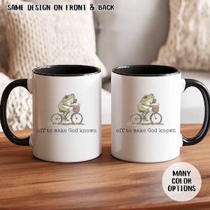 May include: Two white ceramic mugs with black rims and handles. Each mug features a whimsical illustration of a frog riding a bicycle with a basket. The text "off to make God known" is printed below the illustration. The text "SAME DESIGN ON FRONT & BACK" is printed at the top.