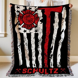 May include: A black and red woven throw blanket with a distressed American flag design. The flag has a red axe and a fire department logo with the text "FIRE DEPT." and the name "SCHULTZ" at the bottom.
