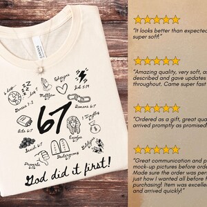 May include: Cream-colored t-shirt with a round neckline, featuring black graphic illustrations and the text "67 God did it first!". The design includes religious symbols and references to biblical verses. A silver necklace with a pendant is visible.