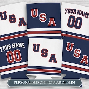 May include: A collection of white and navy blue can coolers with red accents. Some coolers display "USA" in red block letters, while others feature "YOUR NAME" and the number "00". The text "PERSONALIZED ON REGULAR OR SLIM" is also visible.