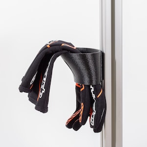 Puede incluir: Un soporte para guantes de plástico negro montado en un poste plateado. El soporte tiene forma de embudo y tiene un par de guantes negros con detalles naranjas colgando de él.