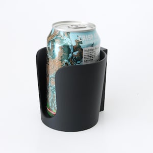 May include: A black car cup holder with a can of beer inside. The can has a blue and green label with the text "CRISP" on it.