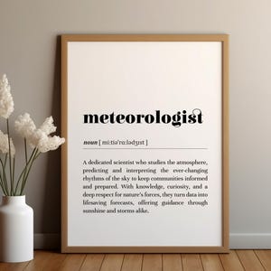 May include: Black and white printable definition of the word "meteorologist" with the pronunciation and a description of the job. The definition is framed in a brown frame and is sitting on a wooden surface.