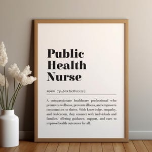 以下が含まれることがあります： 「Public Health Nurse」と黒字で書かれた額入りのプリント。その下に定義があります。プリントの左側には、白い花が入った白い花瓶があります。木製の表面に置かれています。