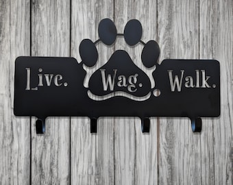 May include: Black metal key hook with three hooks. The hook is shaped like a paw print with the words "Live. Wag. Walk." on it.