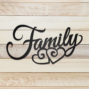 Puede incluir: Decoración de pared de metal negro con la palabra "Family" en una fuente de letra cursiva decorativa. Dos corazones estilizados están debajo de la palabra.