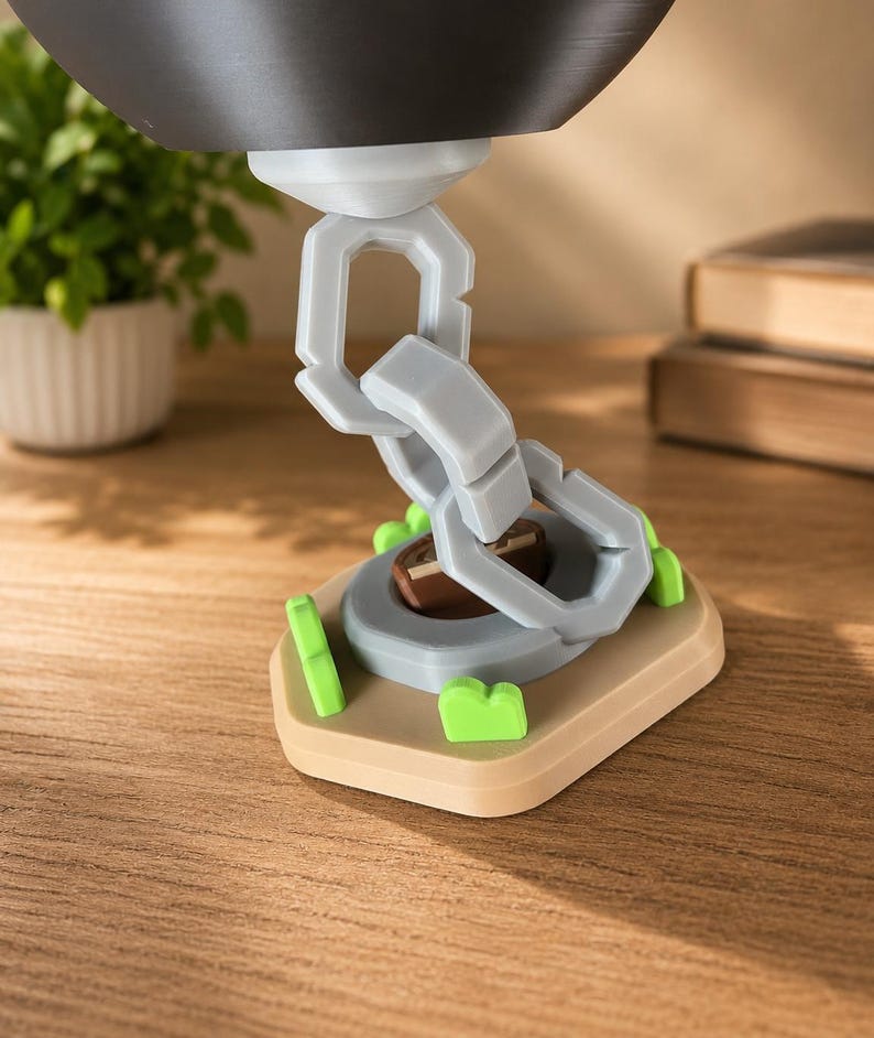 May include: A light gray plastic chain link structure extending upward from a tan base. The base features small bright green accents and a central brown circular element. The chain connects to a dark gray rounded object at the top of the assembly.