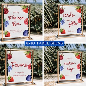 May include: Four 8x10 inch table signs in gold frames. Each sign has a white background with watercolor illustrations of strawberries, raspberries, and blueberries. Text on the signs includes "Mimosa Bar", "Cards and Gifts", "Favors", and "Custom Sign".