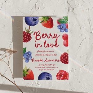 May include: A rectangular invitation with a white background, featuring watercolor illustrations of strawberries, blueberries, and raspberries. The text "Berry in love" is written in red script, with additional details about the event and the bride's name.