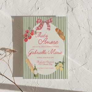 K&ouml;nnte beinhalten: Einladung zur Brautparty mit dem Text "That's Amore" in roter Schrift. Die Einladung zeigt Illustrationen von Tomaten, einem Baguette, Pasta, Zitronen und einer Weinflasche. Der Hintergrund hat gr&uuml;n-wei&szlig;e Streifen.
