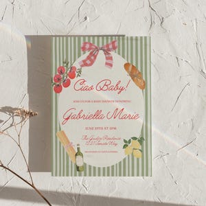 May include: Baby shower invitation with a green and white striped background. The invitation features a central oval design with the text "Ciao Baby!" and "Gabriella Marie." Illustrations include tomatoes, a baguette, lemons, and pasta.