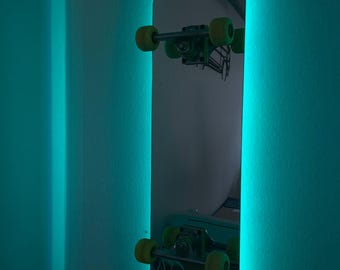 May include: A skateboard-shaped mirror with a neon teal border mounted on a wall. The skateboard has yellow wheels and green trucks. The wall is painted a teal color.