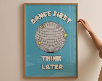 May include: A framed poster with a light blue background and a disco ball graphic. The text "DANCE FIRST THINK LATER" is displayed in a retro font. The frame is a light brown color.