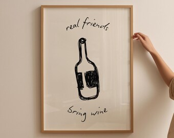May include: A framed art print featuring a black sketch of a wine bottle. The words "real friends" and "bring wine" are handwritten in black ink. The frame is a light brown color.