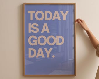 May include: A framed poster with the words "TODAY IS A GOOD DAY" in beige letters on a blue background. The frame is a light brown color. A person's hand is touching the frame.