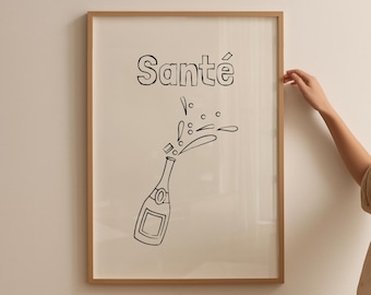 May include: A framed print featuring a black and white illustration of a champagne bottle with the word "Santé" above it. The champagne bottle is depicted with bubbles and a splash, suggesting a celebratory theme.