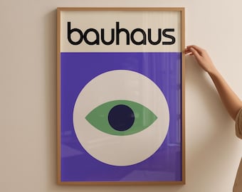 May include: Framed Bauhaus art print featuring the word "bauhaus" in black letters above a purple rectangle. Below, a white circle contains a green eye with a dark blue pupil. The artwork is in a wooden frame.