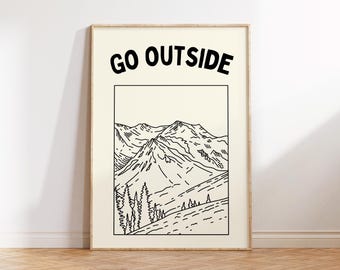 May include: A framed art print featuring a black and white mountain landscape illustration. The words "GO OUTSIDE" are printed in bold, black letters at the top. The artwork is set against a cream-colored background, framed in a light wood.