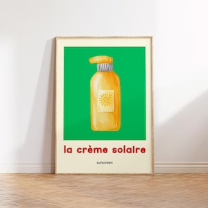 May include: Framed poster with a watercolour illustration of a yellow sunscreen bottle on a green background. Text reads "la crème solaire" and "sunscreen" in red and black. The image is in a wooden frame.