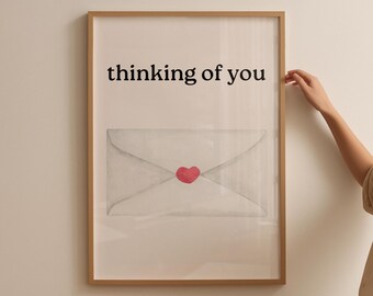 May include: Framed art print featuring the text "thinking of you" above a watercolor illustration of an envelope sealed with a red heart. The artwork is in a wooden frame.