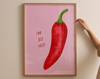 May include: A framed art print featuring a vibrant red chili pepper with a green stem against a pink background. The text "I'M SO HOT" is printed in red. The frame is a light brown color.