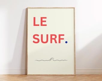 May include: A framed poster with the words "LE SURF." in red, with a blue dot and a black wave illustration. The poster has a cream-colored background and a wooden frame, leaning against a white wall.