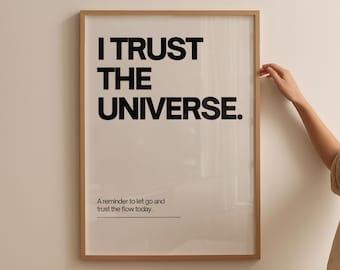 May include: Framed art print with the text "I TRUST THE UNIVERSE" in bold black letters. Below the main text is the phrase "A reminder to let go and trust the flow today." The frame is a light brown color.
