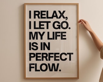 May include: A framed print with the words "I RELAX, I LET GO. MY LIFE IS IN PERFECT FLOW." in bold black letters. The frame is a light brown color, and the background is a neutral off-white. The image is hanging on a white wall.