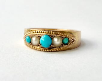 May include: A gold ring featuring a marquise-shaped setting with a beaded border. The center is adorned with a row of five stones, alternating between three round turquoise cabochons and two round white pearls, set horizontally in the band.