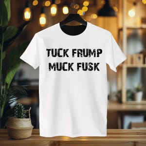 May include: White t-shirt with black text that reads "TUCK FRUMP MUCK FUSK".
