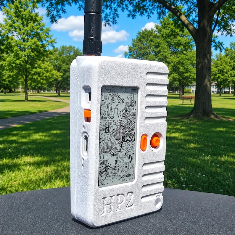 May include: A white handheld radio device with a textured finish, featuring a black antenna, a vertical screen displaying a map, and orange buttons. The front of the device is embossed with the text HP2, and it includes a side-mounted orange switch.