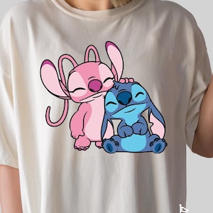 May include: A white t-shirt with a pink and blue cartoon character design. The characters are Stitch and Angel from the Disney movie Lilo & Stitch. The text "MICKEY" is printed at the bottom of the shirt.