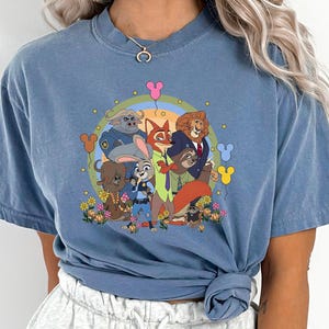 May include: Blue jean colored t-shirt featuring a colorful cartoon graphic of animal characters. The graphic includes a rainbow, flowers, and balloon-shaped designs. The text "BLUE JEAN" is printed at the bottom of the shirt.