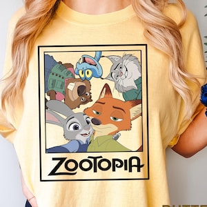 May include: Yellow t-shirt featuring a rectangular graphic of characters from the animated film Zootopia. The graphic includes Judy Hopps, Nick Wilde, and other characters. The word "Zootopia" is printed in black at the bottom of the graphic.